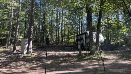 Campsite view showing an RV on a cleared site with pedestal hookups and wooded surroundings — good depiction of actual RV/campsite layout from the Layout page.
