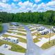 Aerial view of RV campground with parked RVs on paved sites, green grass, and trees.