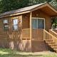 Exterior cabin on-site: clear photo of a wood cabin with porch/steps and neighboring RVs visible, suitable for the cabins listings (appears on the Cabins and Activities pages).