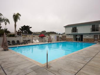 The swimming pool and spa during the daytime, featuring lounge chairs, matching seating with adjoining tables and umbrellas for shade.
