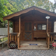 Small brown cabin with a front porch, centered front door, and gravel path in a wooded setting