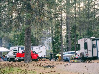 RV campsite scene showing multiple full‑hookup RVs, picnic setup and trees — clearly depicts the resort’s RV camping area and site character (from Accommodations page).