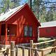A sunny day illuminates Patterson Guard Station. The bright red color of the Guard Station contrasts the green conifer trees behind it. 