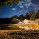 Clean spring-fed lake at evening at Sleepy Hollow Campground with activity center, chairs, and lights in background.
