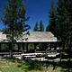 Large, covered picnic pavilion near an open meadow in a pine forest under deep blue sky.