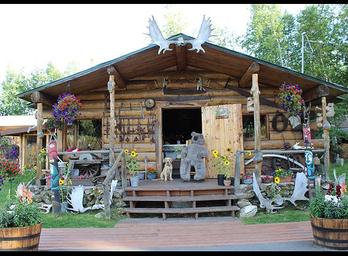 Log cabin storefront with outdoor decorations, moose antlers and planters — clear photo of the Tatlanika gift shop/building shown on the site, useful as a facility shot for the campground/gallery.