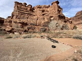 Group campsite with picnic tables, fire pit, and grill, cliffs in background.