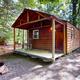 Close photo of a rustic cabin with porch, wooded setting and fire ring — useful to illustrate cabin accommodations and woodsy campsite atmosphere from the site’s Cabins section.