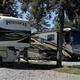 Close view of large RVs on gravel pads beneath trees — demonstrates typical full-hookup big-rig sites advertised on the property pages (slide of sites).
