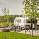 Close view of RV slip/parking pad with picnic table, fire ring and lake in background — clear depiction of RV campsites and site amenities.