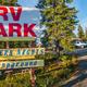 Clear daytime entrance sign reading 'RV PARK / Northern Nights RV Campground' with parked RVs and trees behind — identifies property access and parking area; located on the homepage.