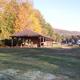 Pavilion pictured on a mown field with nearby RV sites and trees — good overall view of a central facility/amenity on the campground.