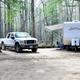 Clear photo of an RV and truck parked in a wooded campsite — shows typical RV pitch and tree cover on the campground. Source page is the campground listing, supporting property relevance.