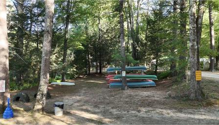 Storage area for canoes/kayaks under trees — highlights available water-activity equipment/facilities and reinforces onsite boating access.