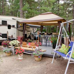 Decorated RV site with canopy, deck, potted plants and adjacent RV — demonstrates upgraded/premium RV site amenities and guest setup featured in the campground’s site photos.