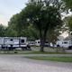 RV area showing multiple RVs, gravel pads and picnic tables with mature trees — useful overview of the RV/RV-hookup sections of the campground as presented on the property's photo gallery.