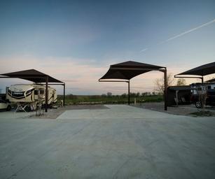 Wide view of multiple RV pads with overhead shade structures and concrete pads — shows the spacious, extra-long RV sites advertised on the Rates page (page: /rates).