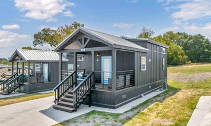 Exterior photo of a standalone cottage on concrete pad with landscaping and nearby RV sites — shows cabin lodging option on the property (homepage/gallery).