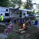 Clear photo of an RV site with camper, picnic table, firepit and surrounding trees — shows typical RV pitch and campsite layout; image appears on the site's home/amenities slider.