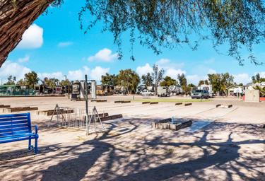 View of RV parking/annual sites and hookups with foreground amenities (bench, fire rings) — illustrates campsite/RV pitch area.