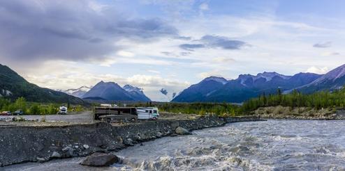 Clear photo of riverfront area with RVs and parking pads — directly shows on-site RV/tent camping and river setting (caption on photos page: ‘Riverfront RV Parking and Tent Camping’).