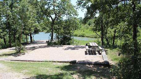 a square campground mostly in sunlight, with a wooden picnic table at the far right. 