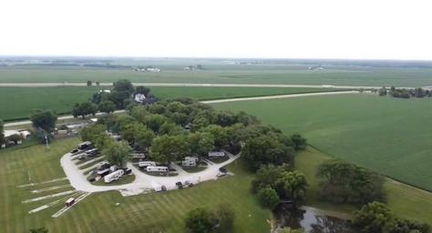 High aerial view showing RV loop, several parked RVs, campground layout, surrounding farmland and a small pond — useful overall overview of the property.