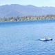 A person on an inflatable raft in a sunlit lake and mountains under a few white clouds floating in blue sky.