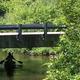 River view with a paddler under a small bridge — good depiction of on-site river access and paddling activity promoted on the campground website.