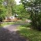 View of a gravel roadway, campsite deck and surrounding tree cover showing campsite layout and wooded setting — useful for illustrating site variety and grounds. Source appears on the site’s main pages.
