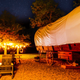 Daytime exterior of a covered wagoneer-style wagon with picnic seating and firepit — clearly depicts one of the glamping units and immediate outdoor amenities (used on The Stays pages).