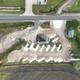 Overhead drone view of a new RV park with empty angled concrete pads, gravel lot, small dark-roofed building, and