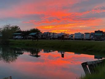 A blazing orange sunset reflected in the park pond, with RVs lined up along the bank