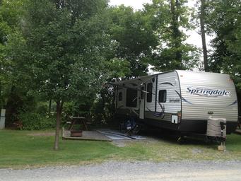 RV parked at a gravel/grass site with picnic table and awning extended — representative photo of RV pitch layout and site amenities found on the campground pages.