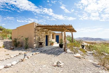 Exterior view of a stone/Adobe-style casita with pergola and surrounding landscape — useful for showcasing individual lodging and site character (from Casitas page).