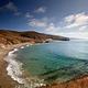 Sandy beach with ocean and small waves and steep coastal bluffs covered in dry grass. 