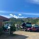 Ground-level view of multiple RVs and vehicles parked on gravel with motel/cabin structure at left and mountains in background — shows RV park layout and site spacing (homepage image).