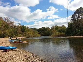 Kayaks on the water and beach at Pulltite under a blue sky with puffy white clouds.