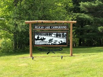 Entrance sign for “Pelican Lake Campground” on grassy frontage — clear identifying shot of the property entrance and branding.