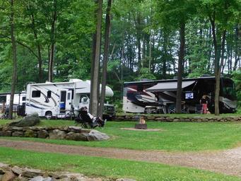 Multiple RVs parked among trees with a central firepit and stonework — illustrates campsite/RV pitch layout and communal fire area (About/Rates pages).