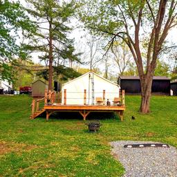 Raised glamping tent on a wooden platform with surrounding grounds and accessory structures — shows cabin/glamp-style lodging available at the campground (page image matches property offerings).