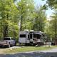 Clear photo of a large RV on a gravel pad among trees — shows an actual RV campsite/pull-through with picnic area; sourced from the campground's 'ways to stay' photo group on the property page.