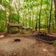 Wooded tent/campsite area with picnic table, fire ring and tree cover — useful for showing tent camping and natural setting (from campground 'ways to stay' photos).