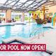 Indoor swimming pool with a pirate ship water feature, rainbow water slides, and lounge chairs, with a bold banner at the bottom reading "New Indoor Pool Now Open!"