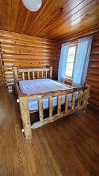 Log bed in log cabin with wood floors and log walls and wood ceiling. 