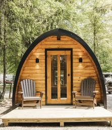 Arched ‘pod’ cabin on a small deck with chairs — highlights alternate cabin accommodation available on the grounds.