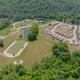 High-angle aerial view showing the pond, parking/entrance and the RV/campsite area — good overall site layout and scale shot from the campground's homepage.