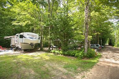 RV campsite among trees with vehicle and gravel roadway — useful view of typical RV/campsite layout (from the rates/reservations campsite gallery).