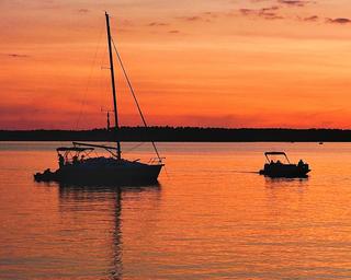 Silhouette of sailboat and small boat at sunset on the water—represents boating activity and waterfront character of the marina property.