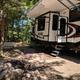 Typical RV site view with large fifth-wheel, picnic table and fire ring — illustrates campsite setup and vegetation on the property (from facilities/services page).